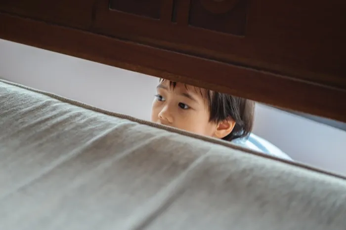 Ein verängstigtes Kind versteckt sich hinter dem Sofa.